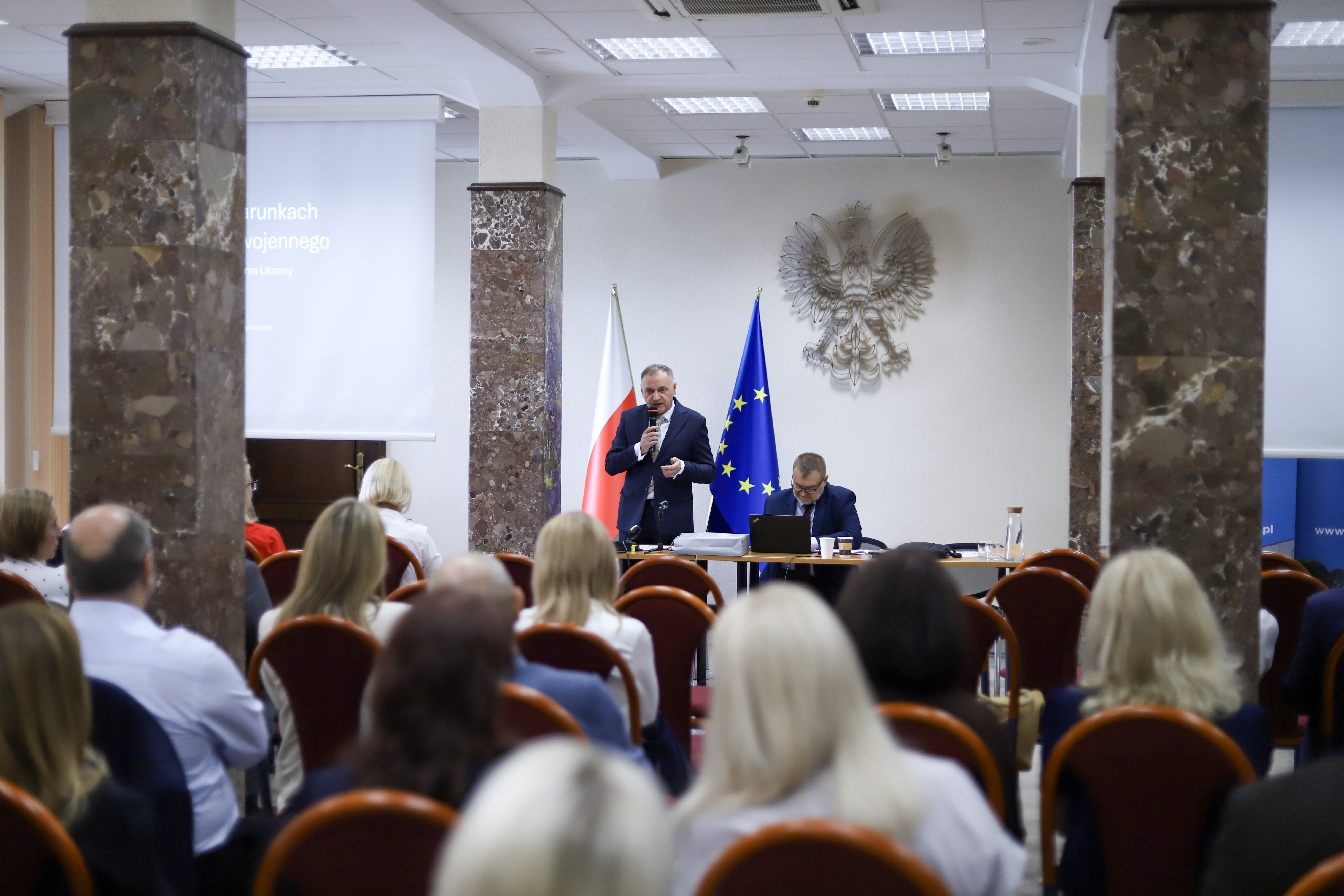 Zdjęcie przedstawia salę konferencyjną, na której z przodu sali znajduje się prowadzący szkolenie oraz tyłem uczestnicy szkolenia