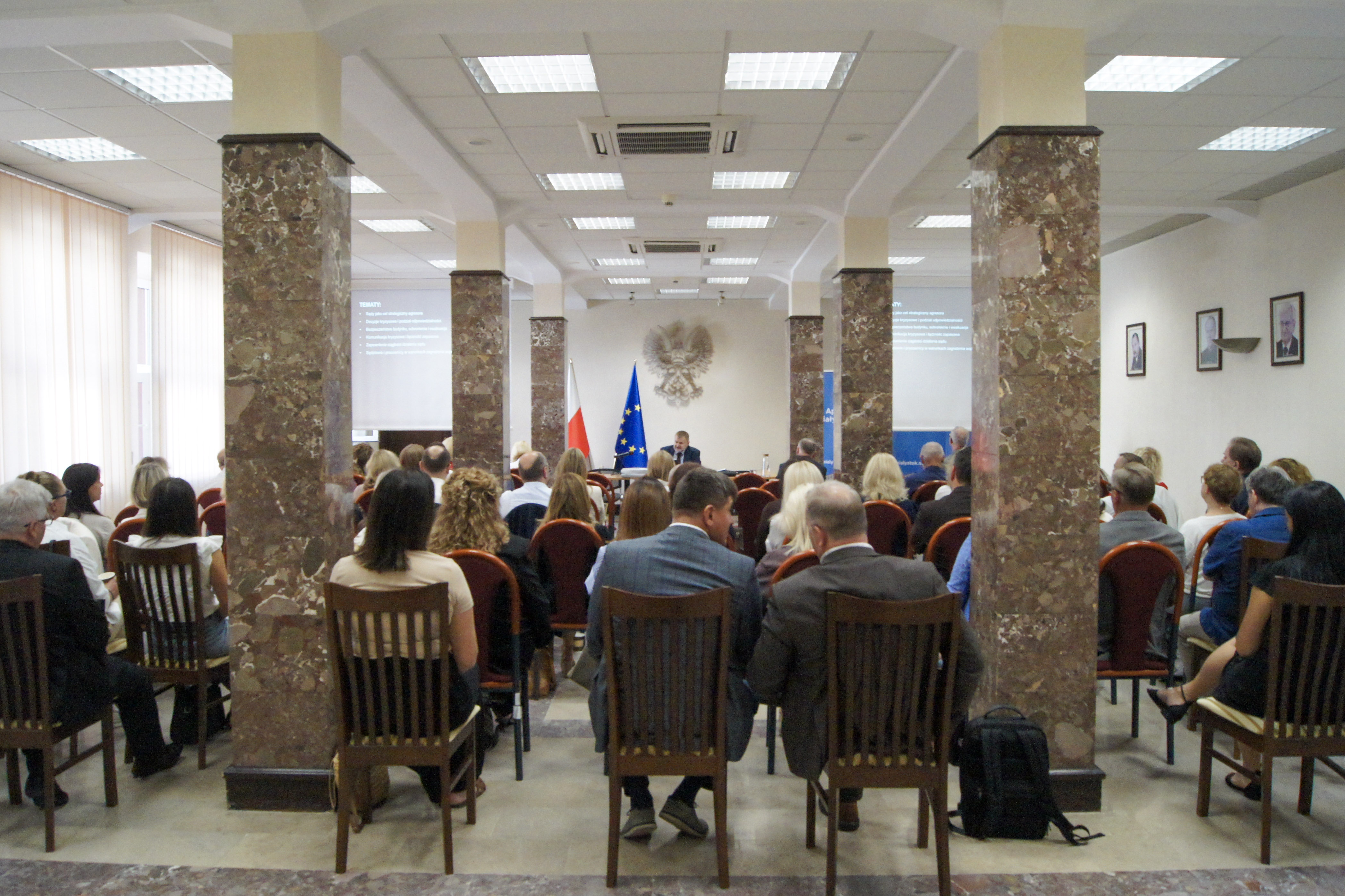 Zdjęcie przedstawia salę konferencyjną, na której z przodu sali znajduje się prowadzący szkolenie oraz tyłem uczestnicy szkolenia.